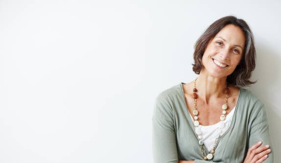 Frau lächelt freundlich mit verschränkten Armen vor hellem Hintergrund.