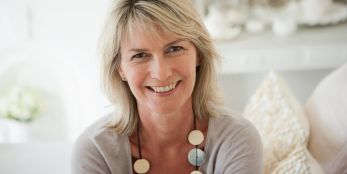 Lächelnde Frau mittleren Alters blickt freundlich in die Kamera.