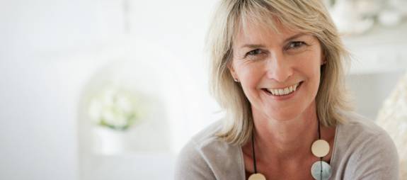 Lächelnde Frau mittleren Alters blickt freundlich in die Kamera.