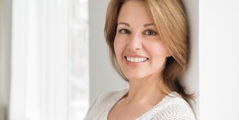 Frau lehnt an Wand und lächelt freundlich in die Kamera.