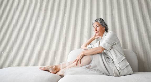 Ältere Frau sitzt entspannt auf Sofa und blickt nachdenklich.