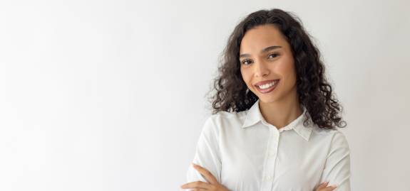 Frau mit lockigen Haaren lächelt selbstbewusst mit verschränkten Armen.