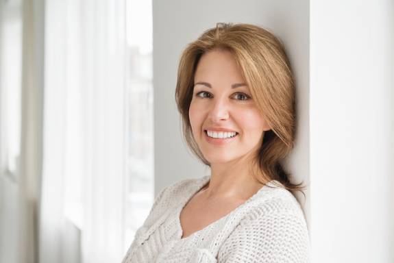 Frau lehnt an Wand und lächelt freundlich in die Kamera.